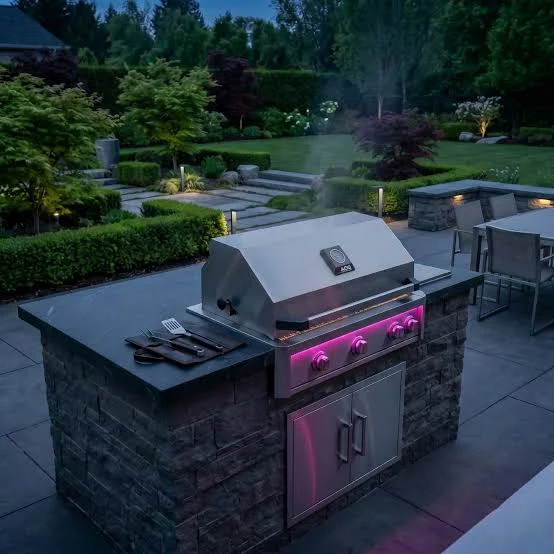 AOG built-in gas grill in a stone outdoor kitchen island with patio lighting at dusk